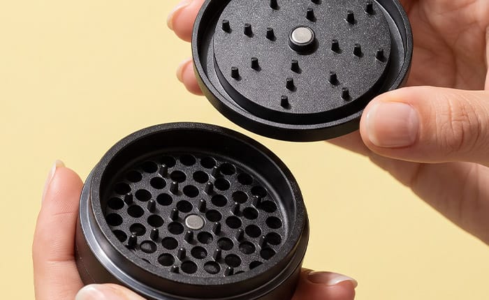 Hands holding the open G Pen dry herb grinder on a pale yellow background